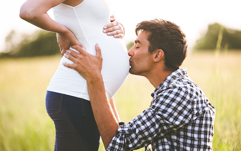 Pregnant Woman With Father kissing her stomach.