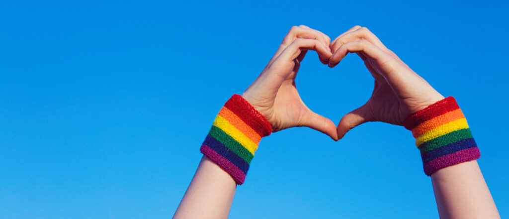 LGBTQIA+ Pride a person holding their hands in a heart with rainbow bracelets on
