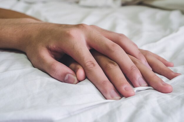 a close up image of two couples holding hands over a white sheet in bed as part of good sexual wellness.